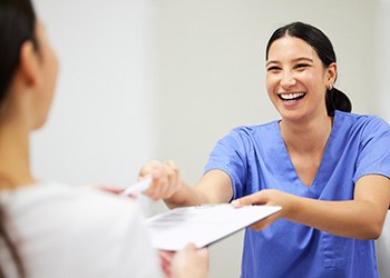 A dentist handing a patient some dental insurance forms