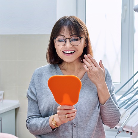 A smiling young woman admiring her dental crown in a hand mirror